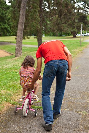 family on bicycle in park - Father helping daughter ride bike Stock Photo - Premium Royalty-Free, Code: 673-03005597