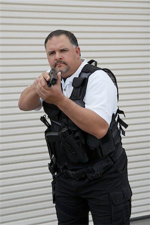 Portrait of security guard in bulletproof vest holding gun Stock Photo - Premium Royalty-Free, Code: 694-03328303