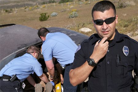 Portrait of police officer, paramedics rescuing car accident victim in background Stock Photo - Premium Royalty-Free, Code: 694-03328551