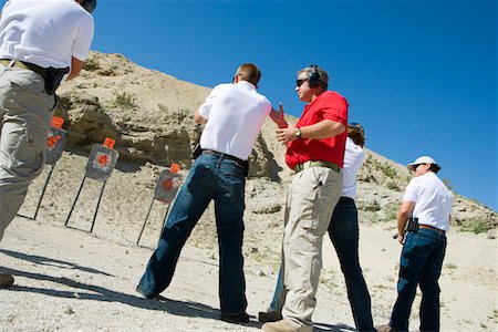 Instructor assisting people aiming guns at firing range Stock Photo - Premium Royalty-Free, Code: 694-03328636