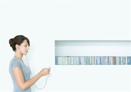 Young woman standing, listening to MP3 player, next to row of CDs, eyes closed Stock Photo - Premium Royalty-Free, Code: 695-05764814