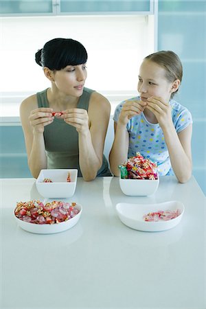 Woman and girl sitting side by side eating bowls of candy Stock Photo - Premium Royalty-Free, Code: 695-05765639