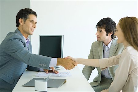 Young couple sitting across desk from businessman, woman shaking hands with businessman, side view Stock Photo - Premium Royalty-Free, Code: 695-05766439