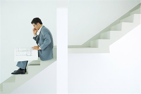 Man in suit sitting on stairs, looking at blueprints, using cell phone Stock Photo - Premium Royalty-Free, Code: 695-05766472