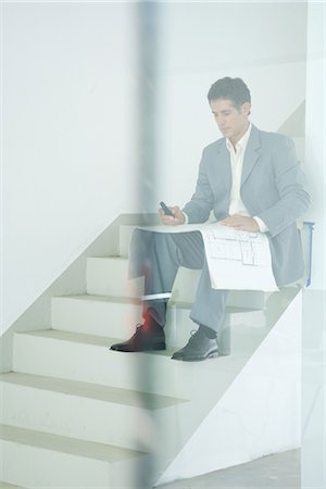 simsearch:6109-06685044,k - Man in suit sitting on stairs, looking at blueprints, using cell phone, seen through glass Stock Photo - Premium Royalty-Free, Code: 695-05766473