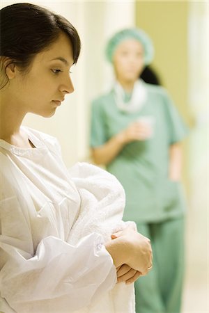 Young woman holding towel in hospital corridor, looking down, medical worker in background Stock Photo - Premium Royalty-Free, Code: 695-05766639