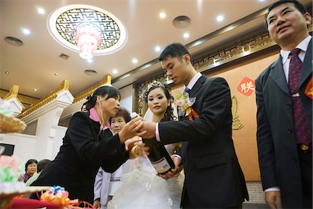 pictures man opening bottle - Woman helping bride and groom open champagne bottle, low angle view Stock Photo - Premium Royalty-Free, Code: 695-05767404