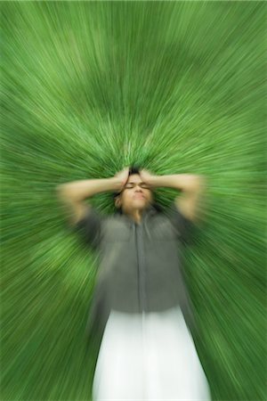 panning (camera technique) - Man lying on back in grass with eyes closed, holding head, blurred motion Stock Photo - Premium Royalty-Free, Code: 695-05767497