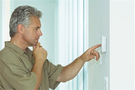 Mature man looking at control panel on wall, hand under chin, side view Stock Photo - Premium Royalty-Free, Code: 695-05767522
