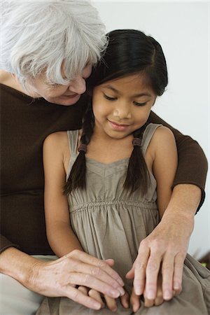 pictures of a little girl whispering - Grandmother embracing granddaughter, holding hands, both looking down Stock Photo - Premium Royalty-Free, Code: 695-05767602