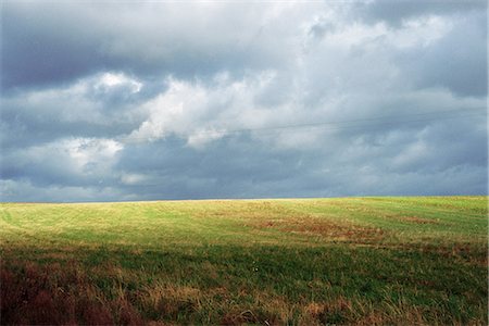 Grassy landscape with storm clouds, power lines in distance Stock Photo - Premium Royalty-Free, Code: 695-05767703