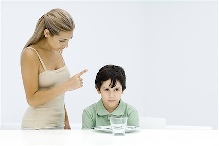 simsearch:695-03380694,k - Boy sulking at table, mother standing beside him, shaking her finger Stock Photo - Premium Royalty-Free, Code: 695-05768031