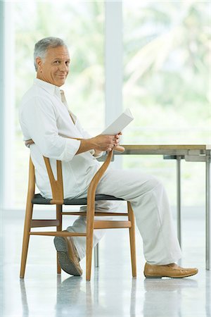 Homme d'âge mûr assis à table, tenant un livre, souriant à la caméra Photographie de stock - Premium Libres de Droits, Code: 695-05768143