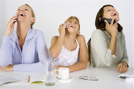 Two women and a preteen girl sitting at table, each using cell phone, all laughing and looking up Stock Photo - Premium Royalty-Free, Code: 695-05768491