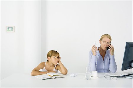 simsearch:695-03380694,k - Woman sitting in front of computer, using cell phone and landline phone, daughter sulking nearby Stock Photo - Premium Royalty-Free, Code: 695-05768842