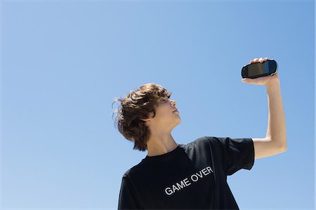 english (people) - Teen boy holding up handheld video game, wearing tee-shirt printed with the words "game over" Stock Photo - Premium Royalty-Free, Code: 695-05768998