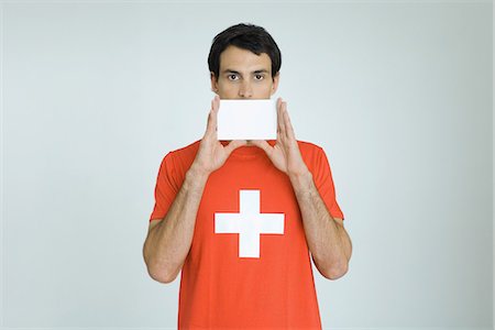 Man wearing Swiss flag tee-shirt, holding blank card in front of mouth Stock Photo - Premium Royalty-Free, Code: 695-05769015