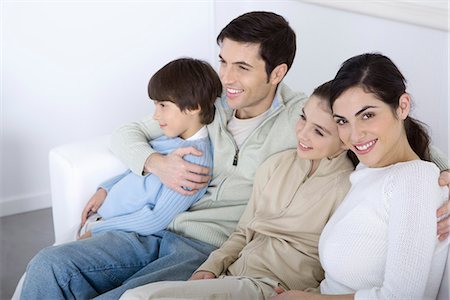 simsearch:695-05769087,k - Family sitting together on sofa, looking away, woman smiling at camera Stock Photo - Premium Royalty-Free, Code: 695-05769089