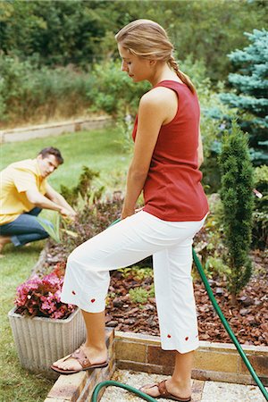 Woman watering garden with hose, husband crouching in background Stock Photo - Premium Royalty-Free, Code: 695-05769708