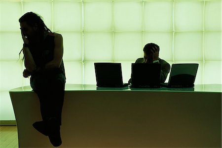 Man with dreadlocks sitting on desk, hand under chin, businessman using laptop computer Stock Photo - Premium Royalty-Free, Code: 695-05769916