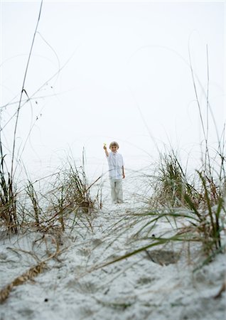 Little boy standing in mid-distance on beach, holding up flower Stock Photo - Premium Royalty-Free, Code: 695-05762836