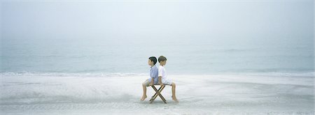 On beach, two boys sitting back to back on stool Stock Photo - Premium Royalty-Free, Code: 695-05762885