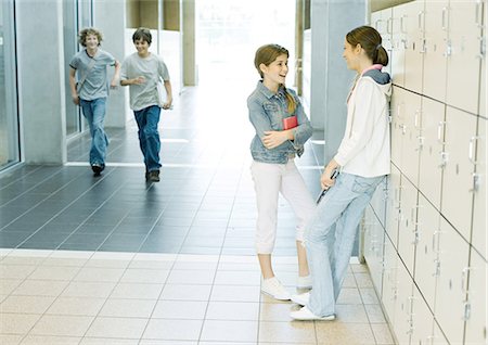 Two teen girls talking by lockers while boys run through hallway Stock Photo - Premium Royalty-Free, Code: 695-05763372