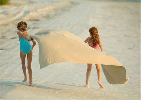 Two girls running on beach, holding blanket out in wind Stock Photo - Premium Royalty-Free, Code: 695-05763597