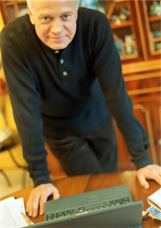simsearch:695-05771662,k - Mature man leaning on desk with laptop, looking into camera. Stock Photo - Premium Royalty-Free, Code: 695-05774702