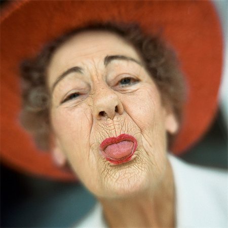 Portrait of senior woman wearing red hat with tongue sticking out Stock Photo - Premium Royalty-Free, Code: 695-05774808