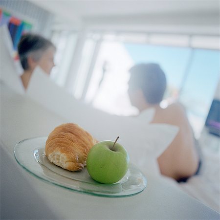 fitness bed - Apple and croissant on plate, people in background Stock Photo - Premium Royalty-Free, Code: 695-05775129