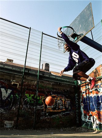 Man hanging on basketball rim after dunking ball Stock Photo - Premium Royalty-Free, Code: 695-05776796