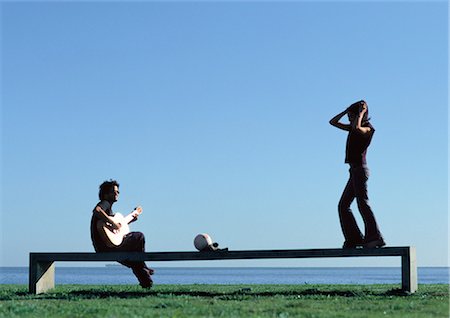 Man playing guitar, teenage girl standing on bench near water Stock Photo - Premium Royalty-Free, Code: 695-05777172