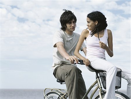 riding bike female basket - Young man sitting on bicycle, young woman sitting on bicycle basket looking over shoulder at young man Stock Photo - Premium Royalty-Free, Code: 695-05777304