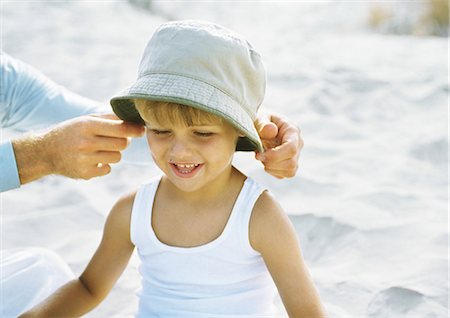 Father's hands putting hat on little boy, on beach Stock Photo - Premium Royalty-Free, Code: 695-05777913