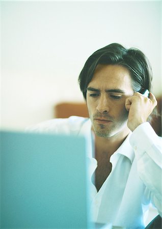 simsearch:6109-06685044,k - Man with serious expression using cellphone while looking at laptop computer Stock Photo - Premium Royalty-Free, Code: 695-05778231