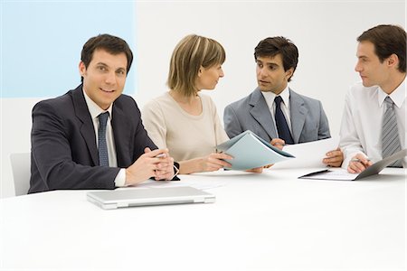 report (written account) - Team of business associates sitting at table, discussing document, one smiling at camera Stock Photo - Premium Royalty-Free, Code: 695-05779243