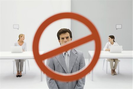 Warning sign across businessman in office, two women sitting with laptops in background Stock Photo - Premium Royalty-Free, Code: 695-05779415