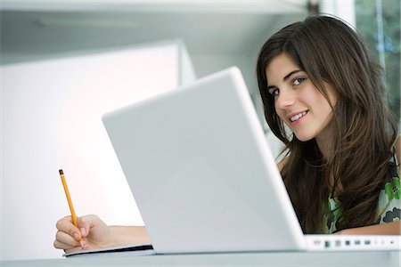 Teenage girl at desk writing, laptop computer in foreground Stock Photo - Premium Royalty-Free, Code: 695-05770536