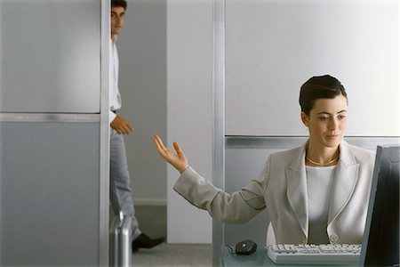 Businesswoman sitting at desk working, motioning for man to enter office Stock Photo - Premium Royalty-Free, Code: 695-05770634