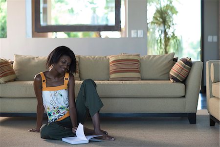 Young woman sitting on living room floor leafing through pages of book Stock Photo - Premium Royalty-Free, Code: 695-05770749