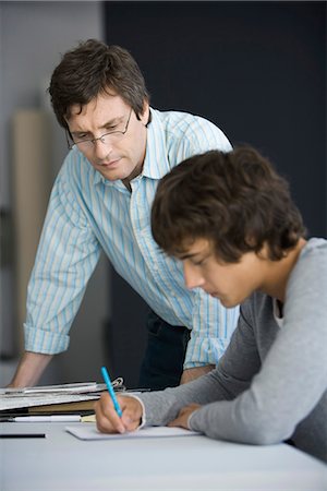 Teacher leaning on desk assisting student in classroom Stock Photo - Premium Royalty-Free, Code: 695-05770807