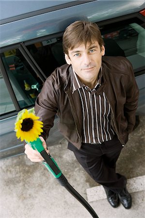 Man at gas station holding gas nozzle with sunflower emerging from end Stock Photo - Premium Royalty-Free, Code: 695-05771084