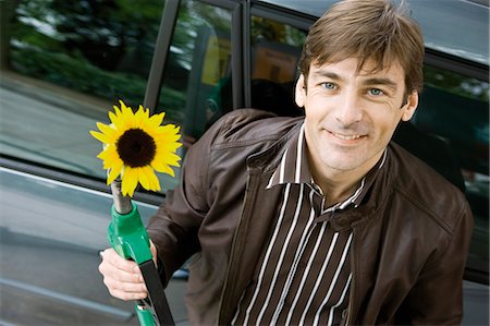 Man at gas station holding gas nozzle with sunflower emerging from end Stock Photo - Premium Royalty-Free, Code: 695-05771085