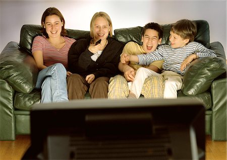 Three young people and one child sitting on green couch together, laughing, blurred rear view of tv in foreground Foto de stock - Sin royalties Premium, Código: 695-05772869