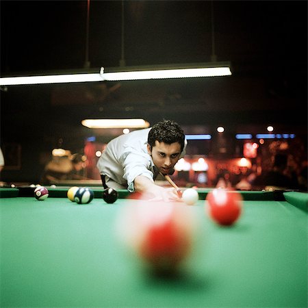 pool party - Young man shooting pool, billiard ball blurred in foreground Stock Photo - Premium Royalty-Free, Code: 695-05773261