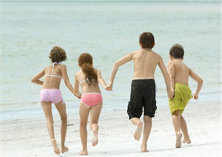 Four kids holding hands and running toward water, on beach, rear view Stock Photo - Premium Royalty-Free, Code: 695-03374027