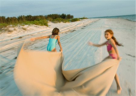 Two girls running on beach, holding blanket out in wind Stock Photo - Premium Royalty-Free, Code: 695-03374050