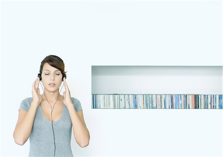 Young woman standing, listening to headphones, next to row of CDs, eyes closed Stock Photo - Premium Royalty-Free, Code: 695-03374647