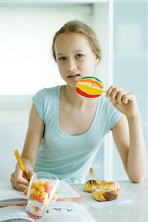 Girl eating sweets and doing homework Stock Photo - Premium Royalty-Free, Code: 695-03375525